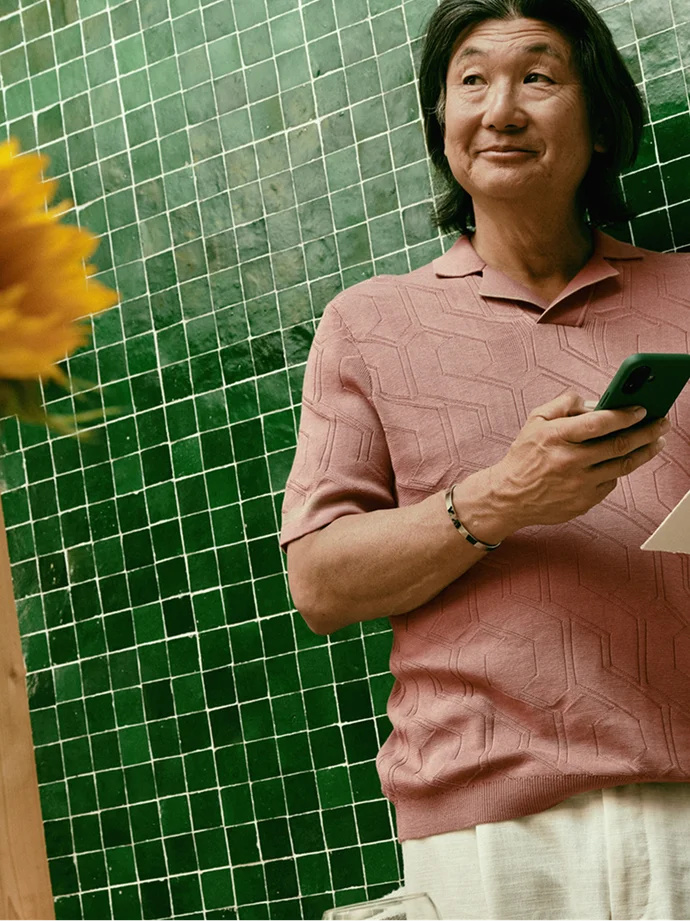 Person with a smartphone in front of a green tiled wall.