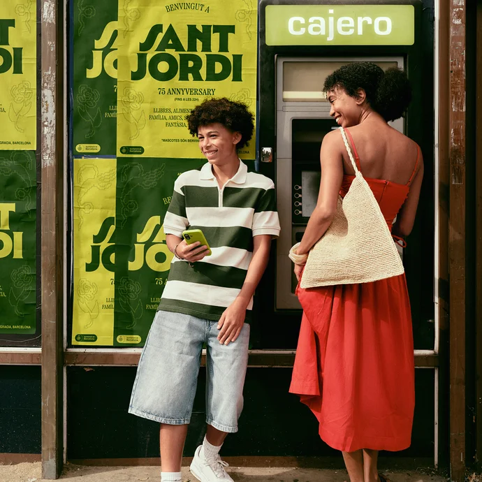 Travellers using a Wise card at a bright green outdoor cash machine.