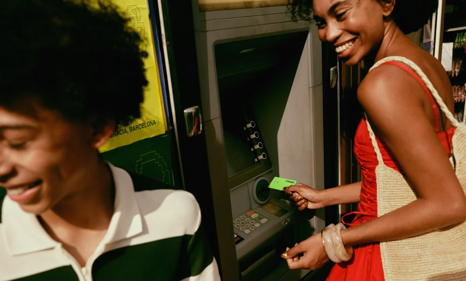 Two smiling travellers using a Wise card at an ATM outdoors.