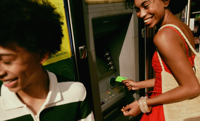 Two smiling travellers using a Wise card at an ATM outdoors.