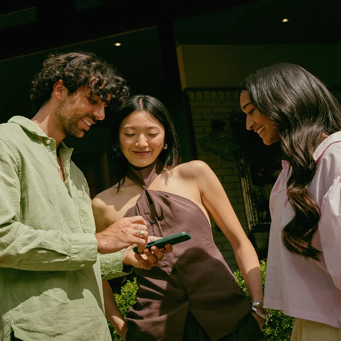 Three friends sitting at a dining table, with one person holding a phone with the Wise app open.