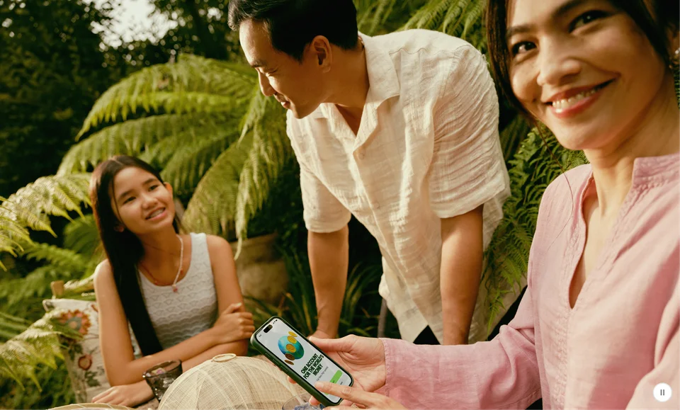 Three smiling friends outdoors; one holds a phone