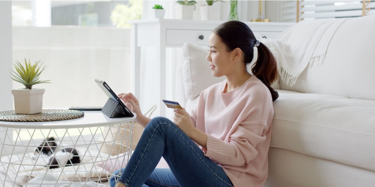 Eine Frau überweist Geld auf einem Tablet und hält eine Bankkarte in der Hand