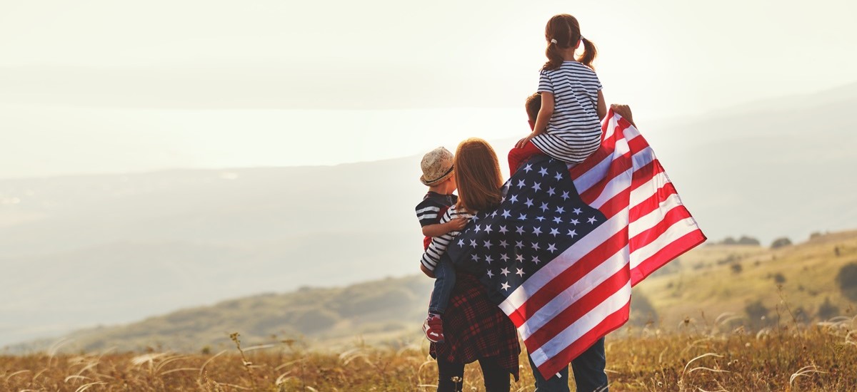 Family wrapped in US flag looking out at Midwest landscape