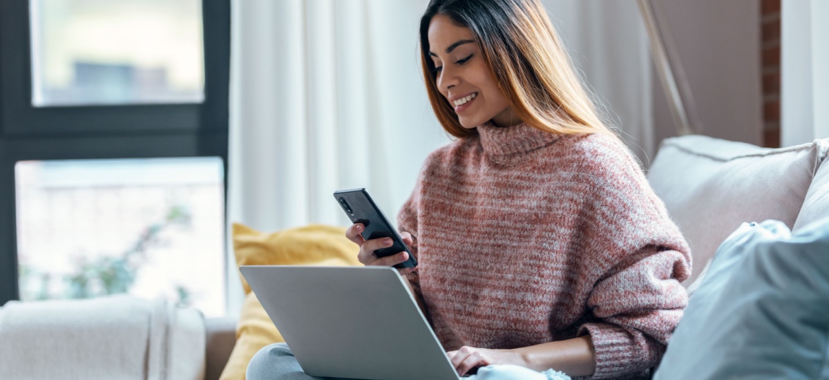 woman-sitting-on-sofa-using-phone-and-computer
