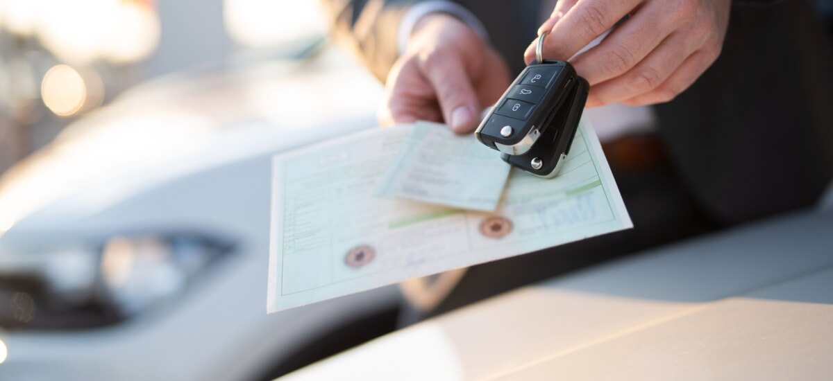 eine Hand übergibt Austoschlüssel und Fahrzugpapiere