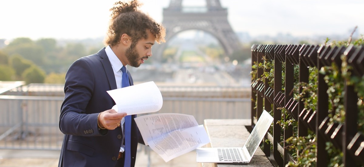 man in suit looking at laptop and holding papers in a rooftop garden with the Eiffel Tower in background