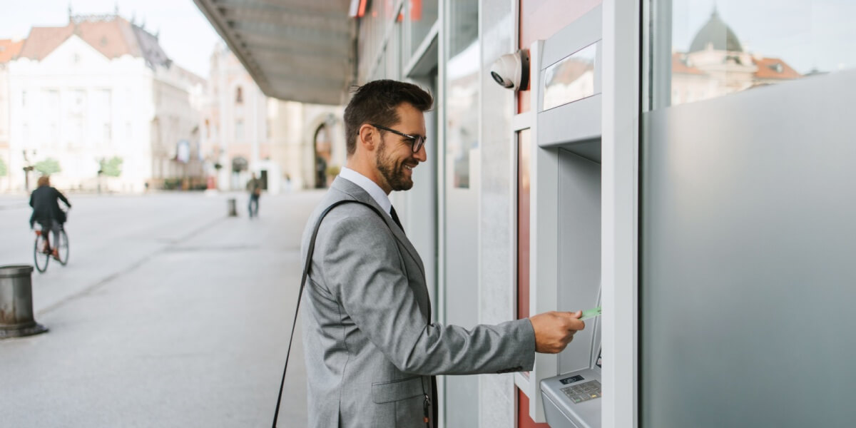 Ein Mann in Anzug hebt Geld an einem Bancomaten ab