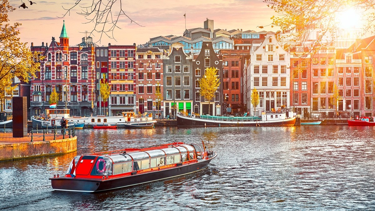 Canal boat on canal in Amsterdam with colourful houses in background