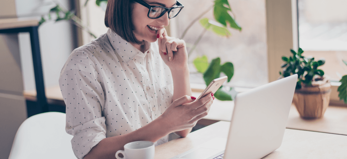 woman-with-laptop-reading-on-phone-in-office