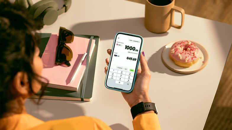 A person sat down with a coffee and donut sending money using the Wise app on their phone.