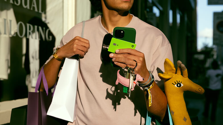 A person holding bags, their keys and a Wise Multi-Currency Card whilst they're outside.